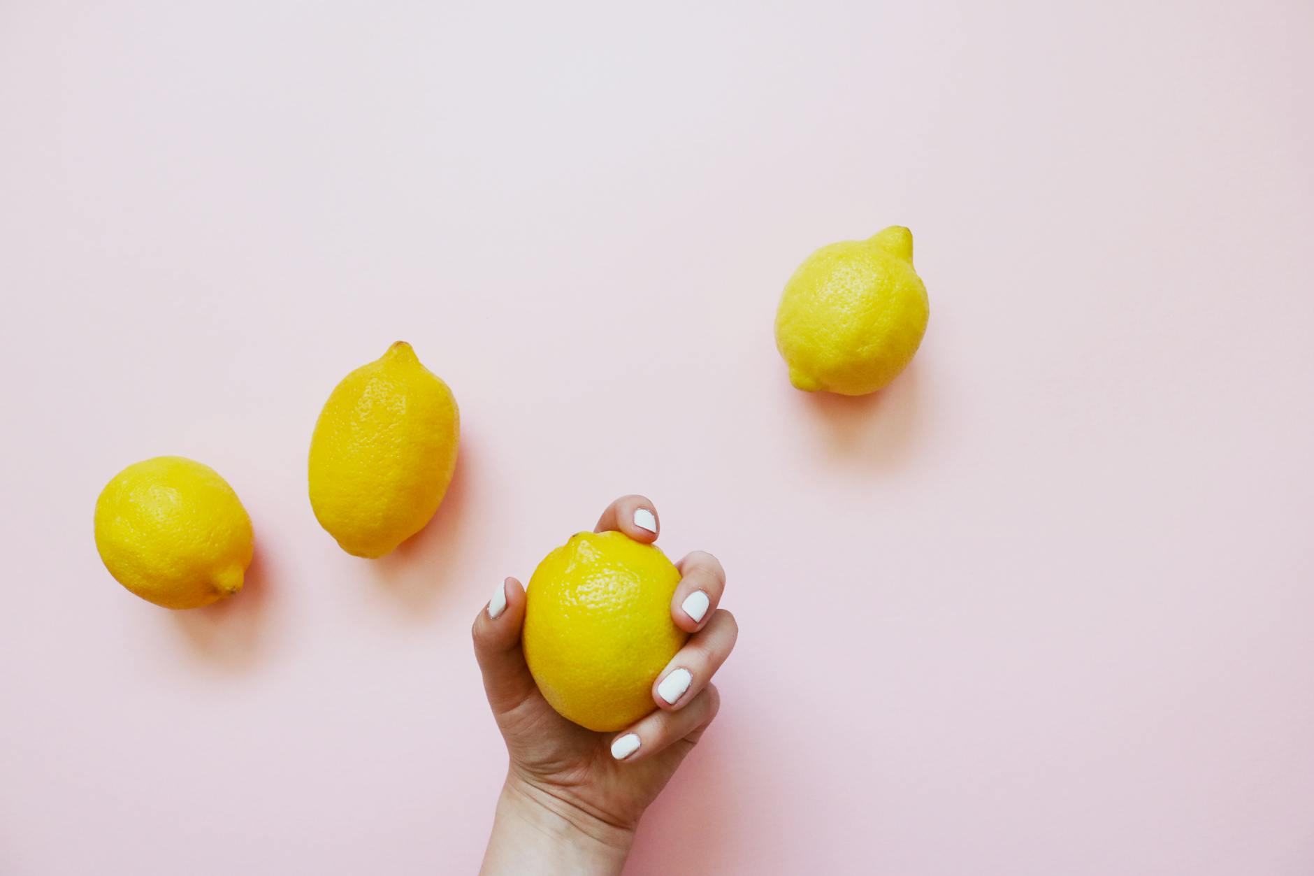 Hand holding a lemon on soft pink background, symbolizing sensitivity and gentleness