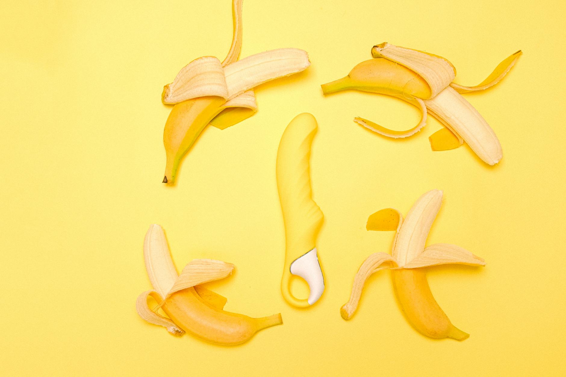 Vibrador de silicona amarillo vibrante rodeado de plátanos pelados sobre fondo amarillo pastel
