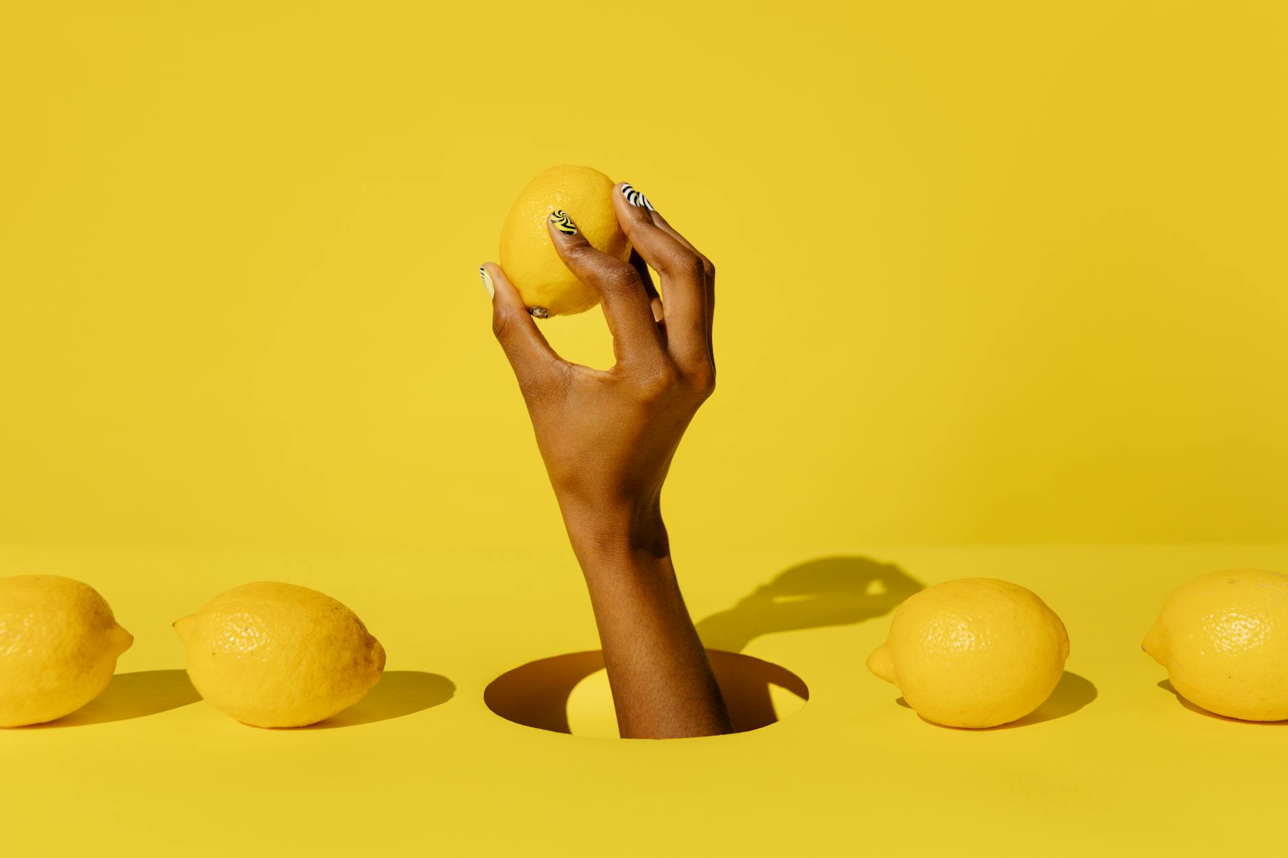 Hand holding a lemon against a bright yellow background, symbolizing fresh sensations