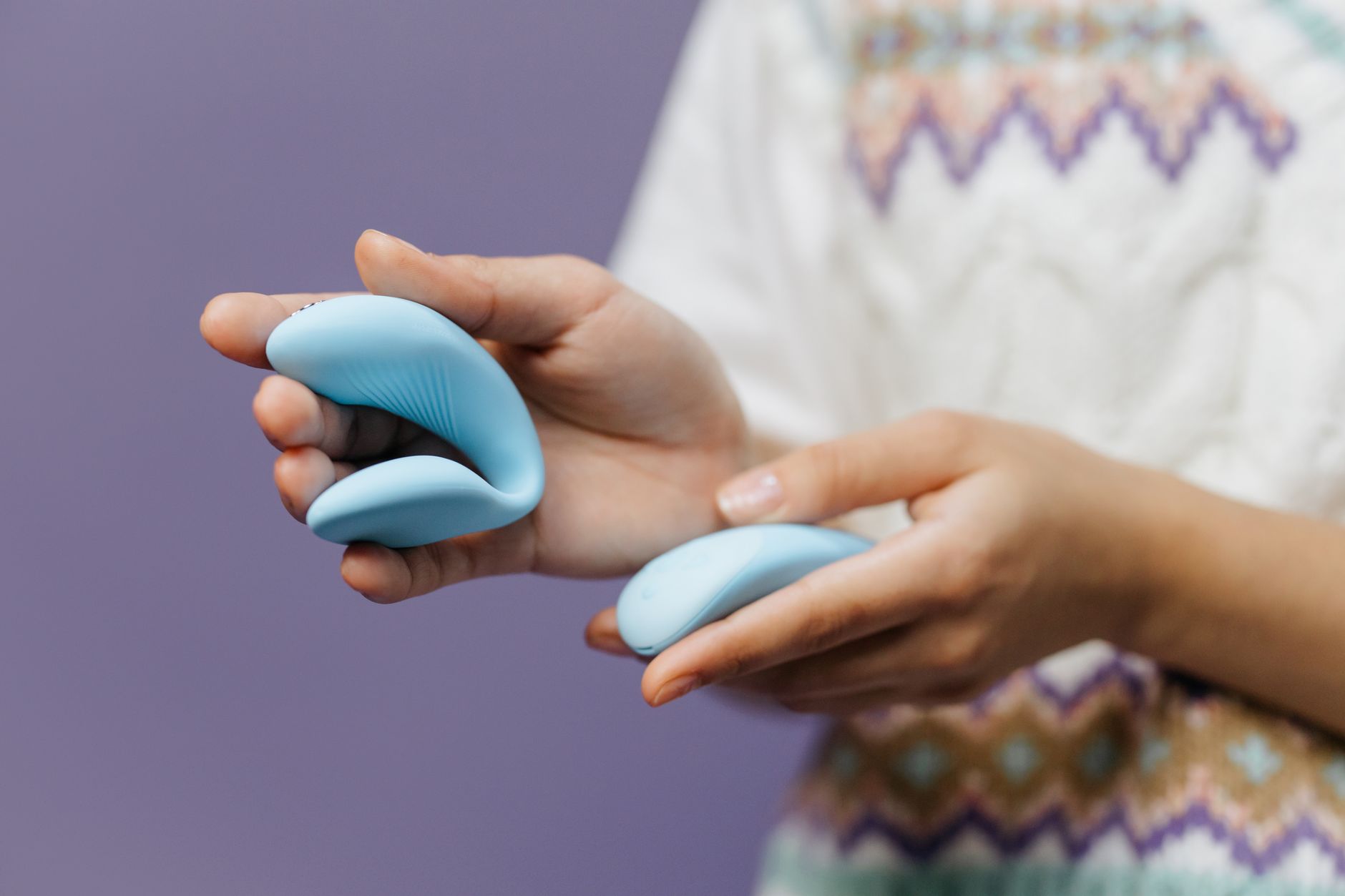 Manos íntimas sosteniendo un vibrador azul contra fondo púrpura