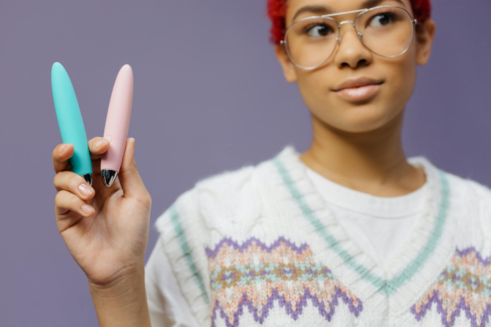 Manos sosteniendo un vibrador personal azul contra un suéter tejido