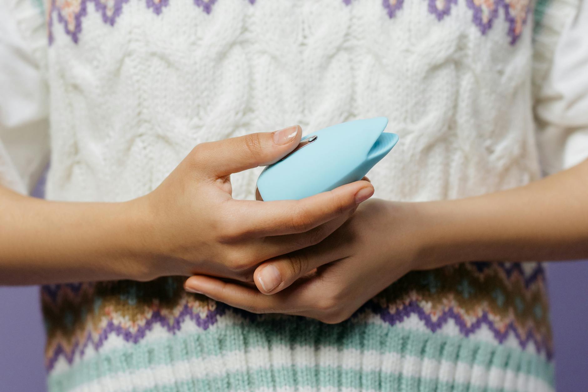 Primer plano de manos sosteniendo un vibrador azul contra un suéter de punto