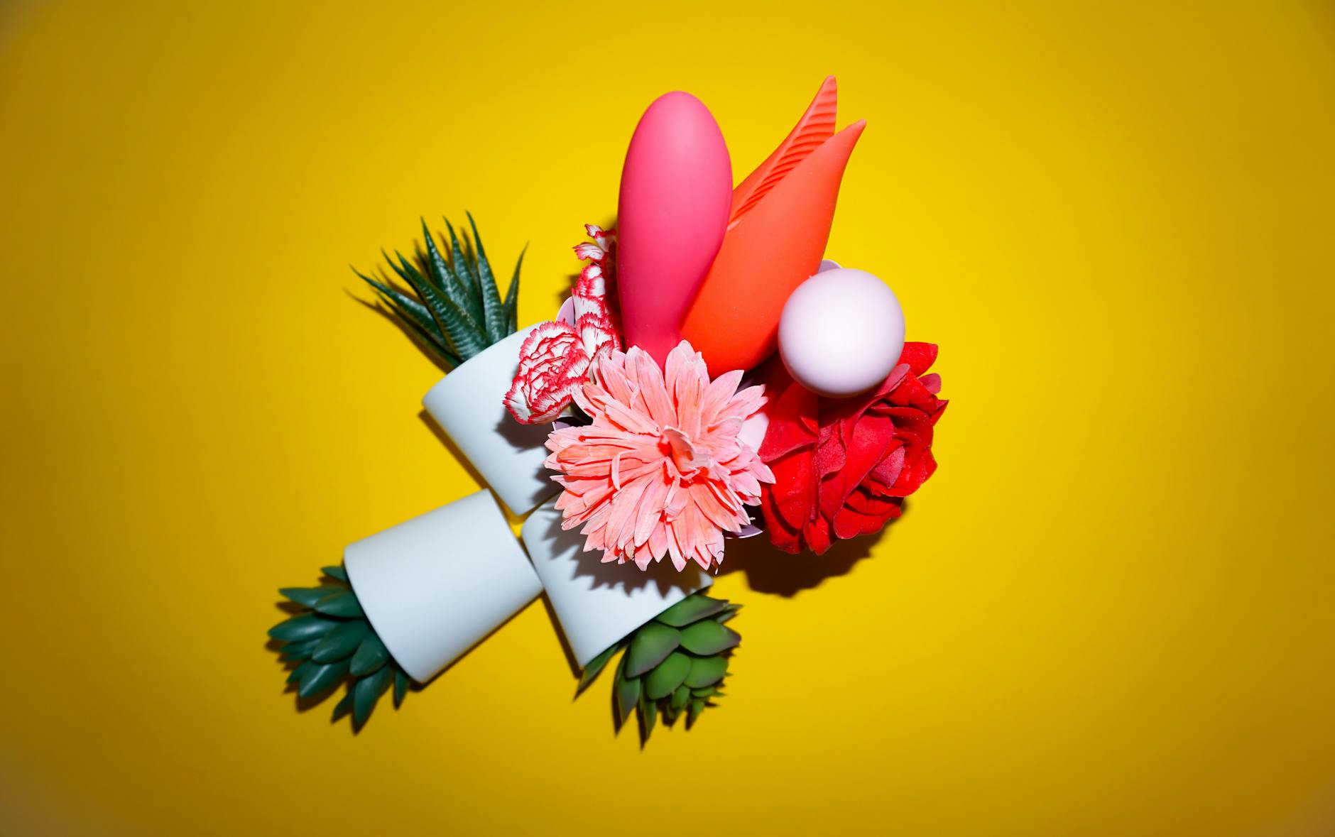 Hands holding pink and blue silicone vibrators against a soft pastel background